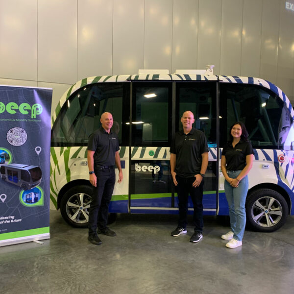 Three people standing in front of an autonomous vehicle.