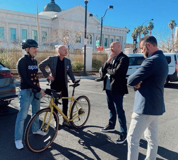 Four men talking holding a bicycle next to a car.