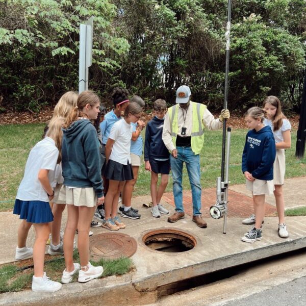 A group of students observing an open manhole in a catch basin